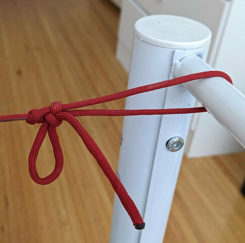 A length of red paracord held taught and looped around a white metal tube.