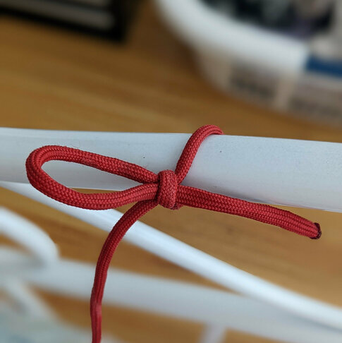 A length of red paracord looped and knotted around a white metal tube.